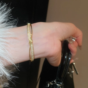Détail d'un bracelet torsadé plaqué or 18K avec zircons, manchette à plumes et sac à main