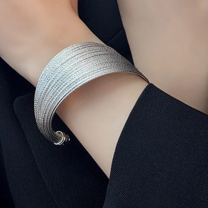 Macro detail of silver layered textured wide cuff bracelet worn over a black blazer
