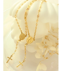 Close-up of gold titanium steel cross and medallion pendant on a white shell prop