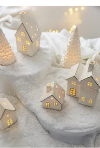 Nahaufnahme von Keramik-Weihnachtshäusern mit warmem LED-Licht und goldenen Verzierungen