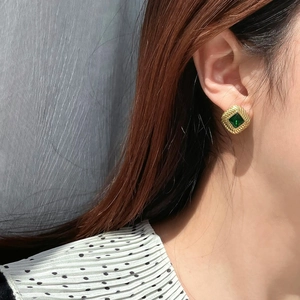 Detailed shot of retro gold square earrings with emerald green zircon and textured bezel