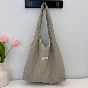 Detail of light sage green pleated tote bag hanging against a wall with flowers