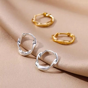 Macro shot of twisted hoop earrings in gold and silver over champagne silk fabric