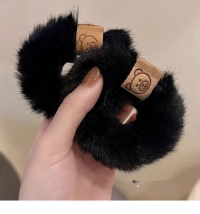 Close-up of black furry scrunchie with cute bear leather tag, soft winter hair accessory.
