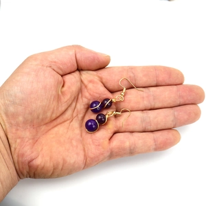Handmade gold wire wrapped purple crystal bead drop earrings held in hand for scale