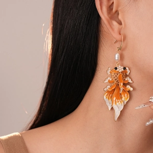 Detail of model wearing koi carp earrings with orange enamel and pearls in warm lighting