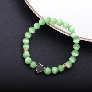 Detail of green cat-eye beaded bracelet with a black heart charm on a leather background