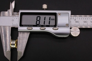 Macro shot measuring an 8.11mm vintage metallic bead with calipers on black background
