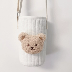 Detail of white quilted water bottle bag featuring a cute beige plush bear embroidery