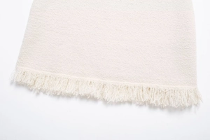 Detailed macro view of off-white tweed fabric texture with decorative fringe hemline