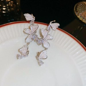 Close-up of silver butterfly drop earrings with sparkling rhinestones on a white plate
