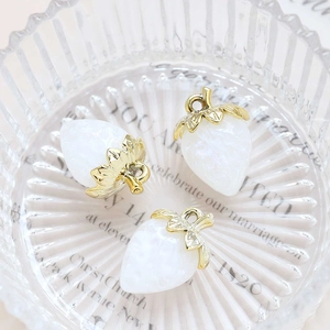 Three white acrylic strawberry pendants with gold metal leaves in a glass bowl for DIY jewelry