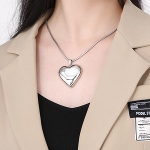 Detail of silver hollow heart pendant necklace worn on neck with sleek snake chain