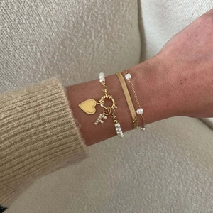 Close-up of stacked gold chain bracelets with pearl accents and an L-letter heart charm