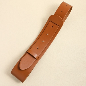 Close-up of a brown leather waist belt featuring a glossy textured finish on beige wall