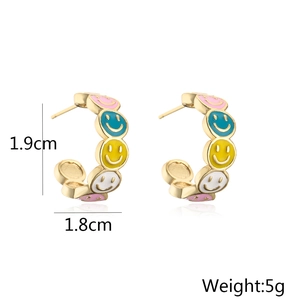 Detail view of 18K gold plated hoop earrings with colorful enamel smiley face patterns
