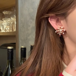 Close-up of elegant red flower pearl stud earring worn by a model in soft warm lighting
