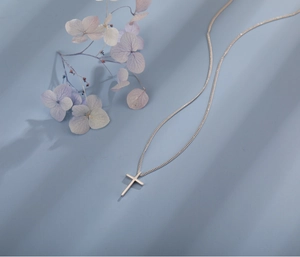 Macro shot of minimalist silver cross pendant on fine chain with matte metallic finish