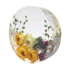 Preserved yellow roses and mixed flowers inside clear circular resin block on white background
