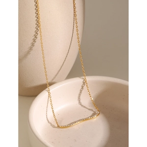 Macro detail of 18k gold plated wave pendant necklace with clear crystals on ceramic