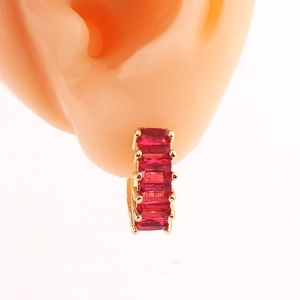 Close-up of a gold hoop earring with red rectangular faceted stones on an ear model