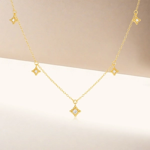 Detail of gold necklace featuring five square pendants with sparkling round zircons