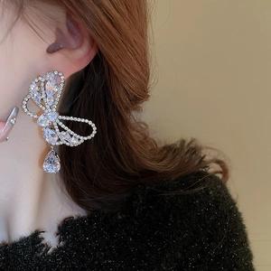 Close-up of sparkling silver bow earrings with drop zircon worn by model