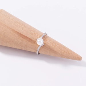 Macro detail of silver wavy ring with central pearl and diamonds on a wooden stand