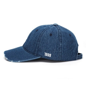 Close-up of white 1999 embroidery on blue denim baseball cap with distressed hole detail