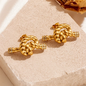 Twisted gold titanium steel earrings with diamond accents on minimalist stone display