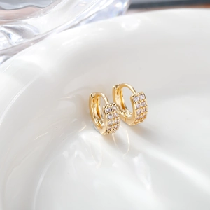 Macro shot of gold zircon earrings with double-row micro-inlay on a white ceramic tray
