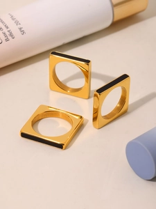 Detailed view of square gold-plated rings with black geometric inlay on modern stands
