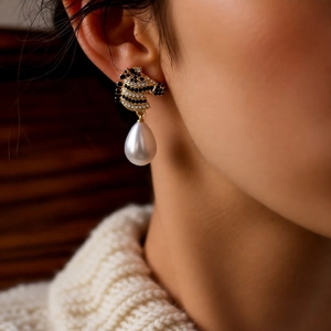 Close-up of zebra head stud earrings with pave crystals and a teardrop pearl on a model