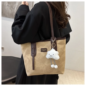 Detail of khaki tote bag with brown straps and white cloud plush pendant accessory