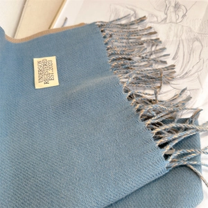 Detail of two-tone blue and beige cashmere-like scarf with tassels and label