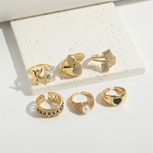 Detailed view of six gold rings with zircons and pearls on white textured stone background