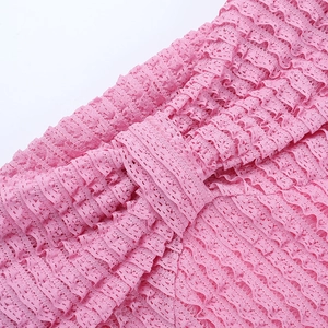 Détail du tissu en dentelle rose avec plis superposés et motifs de maille texturés