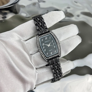 Detail of tonneau-shaped emerald face watch with diamond bezel on a black metal strap