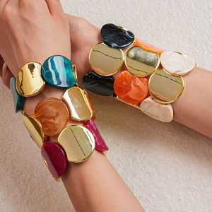 Dettaglio di larghi bracciali boho con dischi in metallo dorato e intarsio in resina colorata