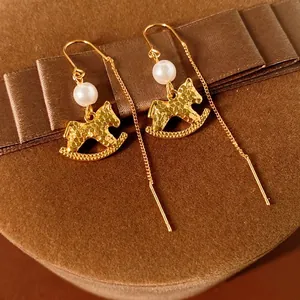 Elegant gold rocking horse drop earrings with pearls on a brown velvet gift box background