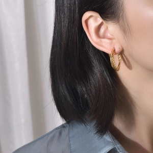 Detail view of golden twisted hoop earrings with a textured design on a model