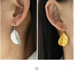 Close-up of elegant leaf-shaped drop earrings with realistic vein texture on a model