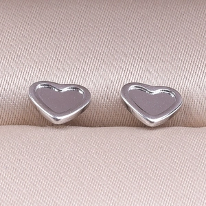 Macro view of silver heart-shaped stainless steel stud earrings on pink satin