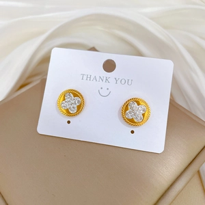 Golden clover stud earrings with sparkling crystals and a textured edge on display card