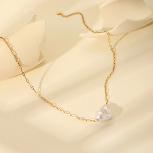 Detail of 18K gold stainless steel chain with a white Baroque pearl pendant on beige stone
