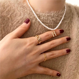 Close-up of gold chain rings and pearl necklace with H letter pendant on a knit background