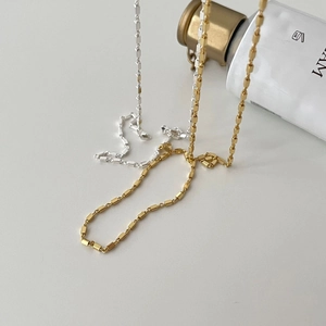 Close-up of gold and silver square link chain necklaces draped on a white background