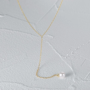 Detail of gold-plated Y-shaped necklace with a white pearl pendant on a grey rock surface