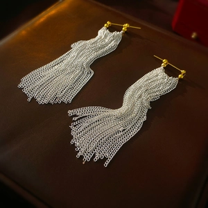 Detailed close-up of metallic long chain tassel earrings on premium leather background