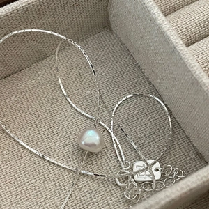 Macro detail of silver pearl necklace featuring a single baroque pearl and adjustable chain
